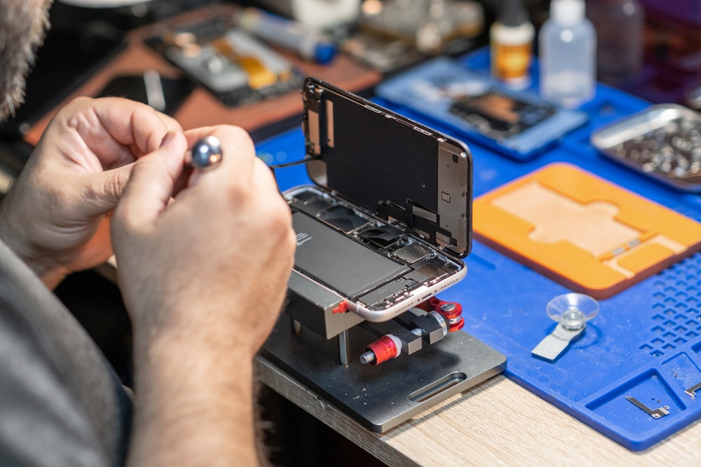 A skilled technician performs phone repair and replaces a battery in a well-organized workshop with tools and parts readily available.