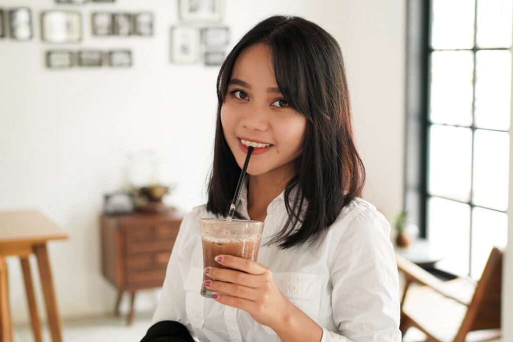 Beautiful young asian businesswoman in suit standing holding brown coffee cup in caffe while having a coffee break.