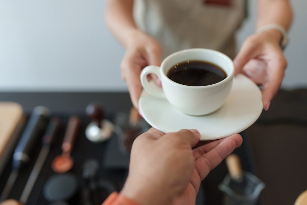 Barista handing a cup of black coffee to a customer in a coffee shop