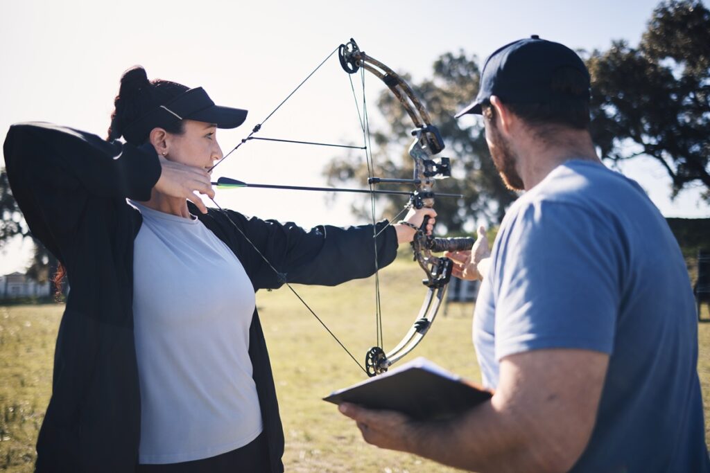 Archery, bow and arrow with woman and coach, aim at target with sports outdoor, combat training and.