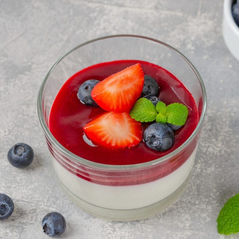 Italian dessert panna cotta in a glass with berry sauce, fresh strawberries and blueberries on top on a gray concrete background. Copy space