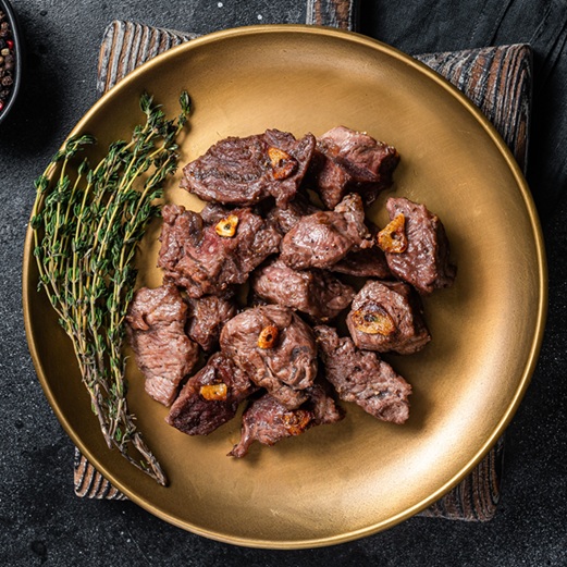 Chopped Grilled Diced Beef garlic steak on a plate with thyme. Black background. Top view