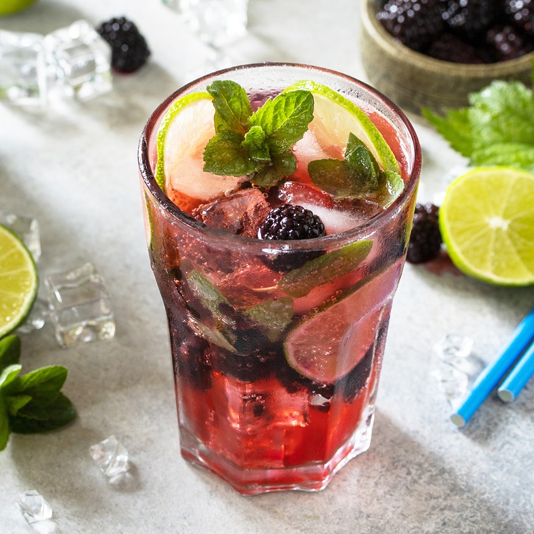 Summer blackberry mojito or blackberry soda. Refreshing summer drink with blackberry, mint, lime and ice on a stone table.