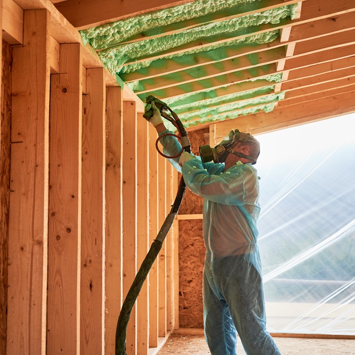 Male builder insulating wooden frame house. Man worker spraying polyurethane foam inside of future cottage, using plural component gun. Construction and insulation concept.
